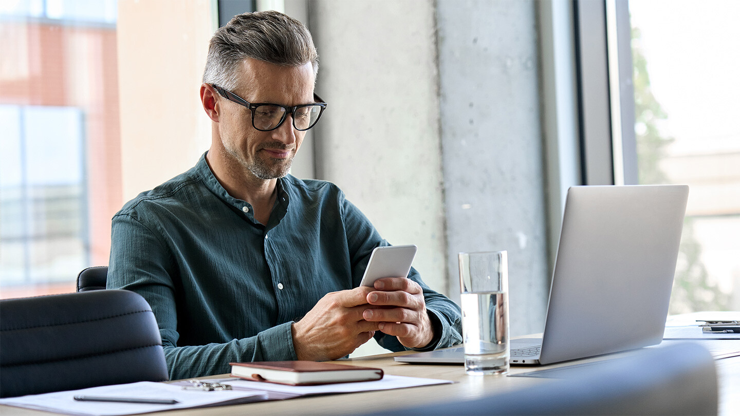 Man at laptop with phone in his hand