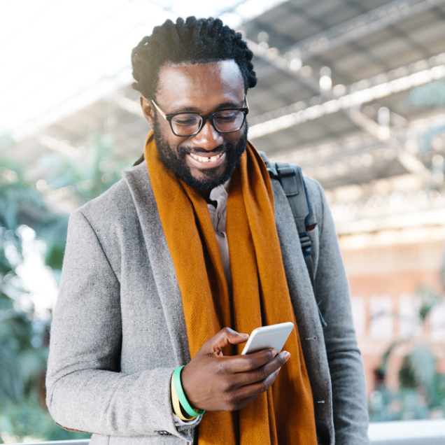 Person wearing a gray coat and orange scarf, holding a smartphone in a bright indoor setting.